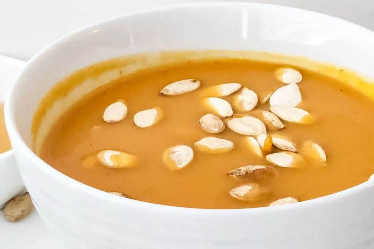 A white bowl filled with orange-colored soup garnished with pumpkin seeds, perfect for lovers of seasonal recipes and delicious squash dishes.
