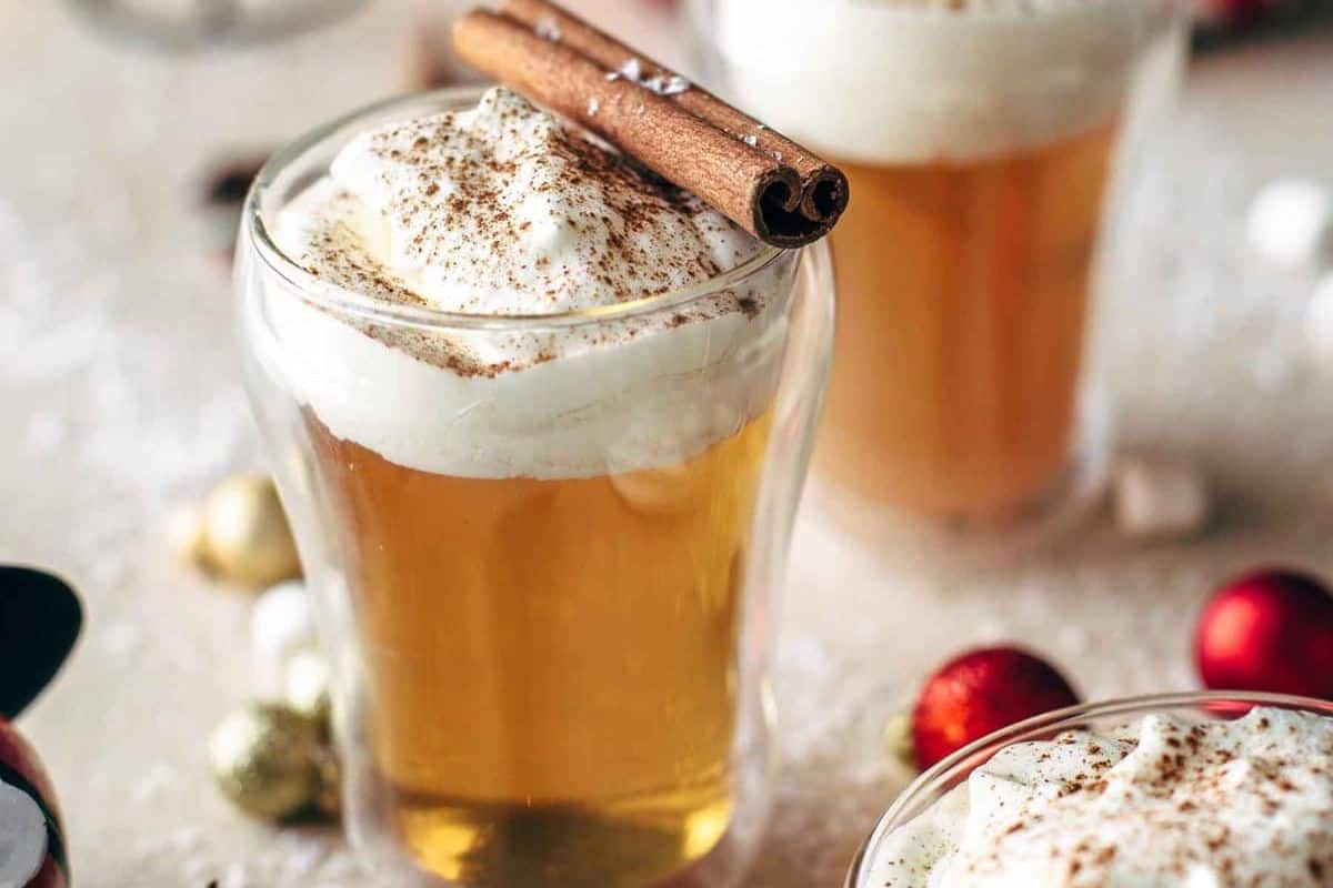 A glass of caramel apple hot toddy cocktail topped with whipped cream and a cinnamon stick.