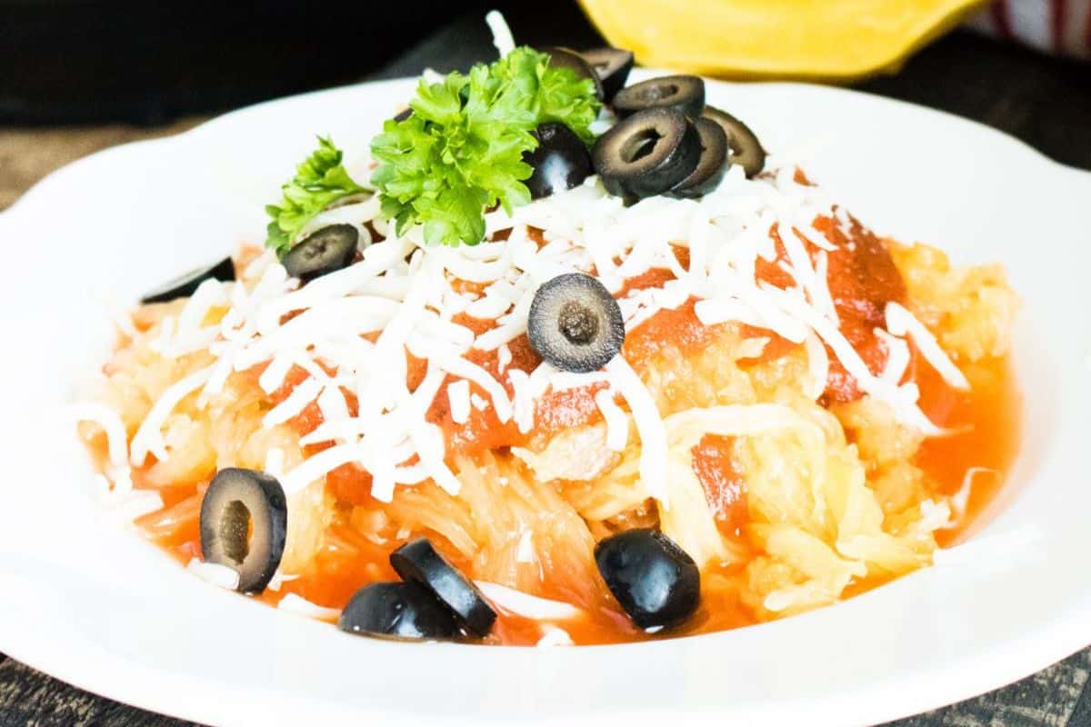 A plate of spaghetti squash topped with tomato sauce, shredded cheese, sliced black olives, and parsley—perfect for lovers of seasonal recipes and squash dishes.