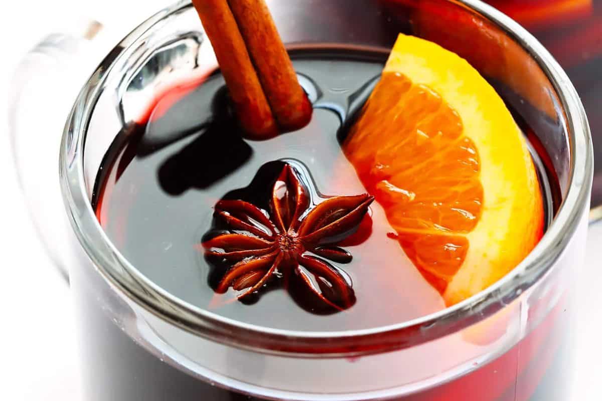 A glass of mulled wine with a cinnamon stick and an orange slice.