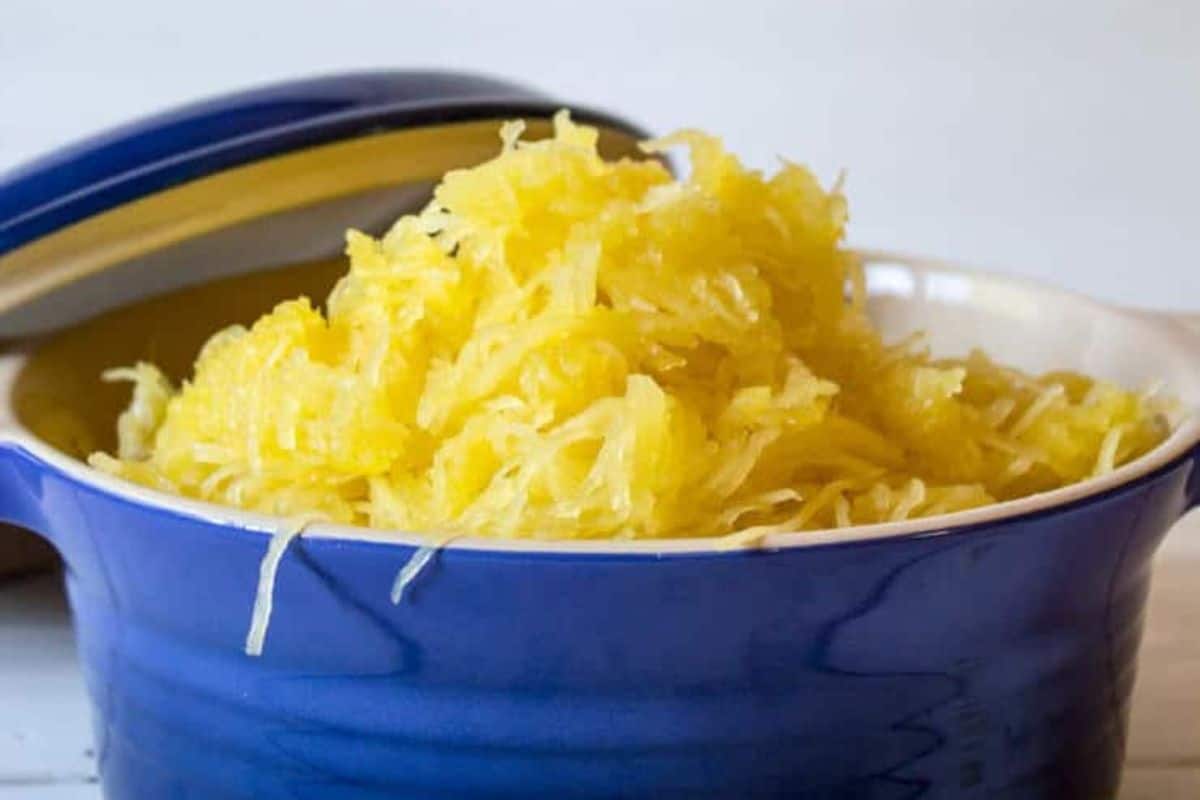 Shredded cooked spaghetti squash is piled in a blue ceramic dish with the lid partially open, making it a standout among squash dishes and perfect for seasonal recipes.