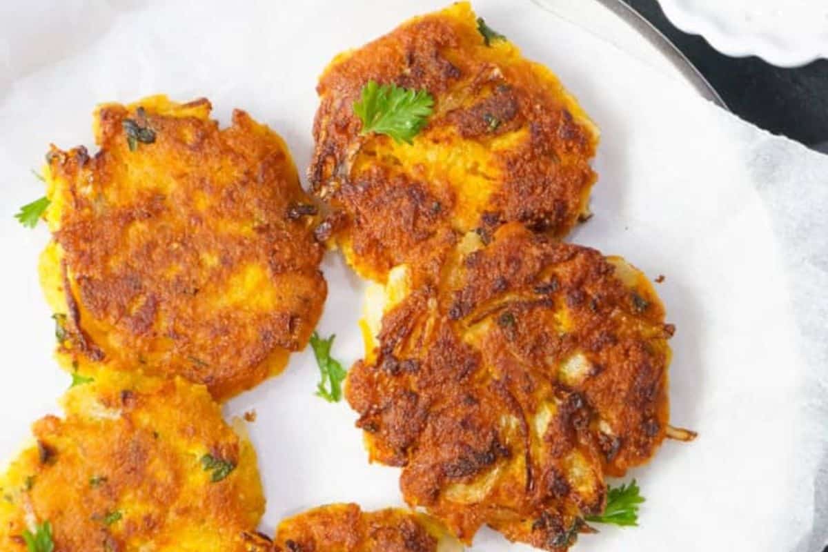 Four golden-brown squash fritters garnished with sprigs of parsley sit on white parchment paper—an inviting treat for fans of seasonal recipes.