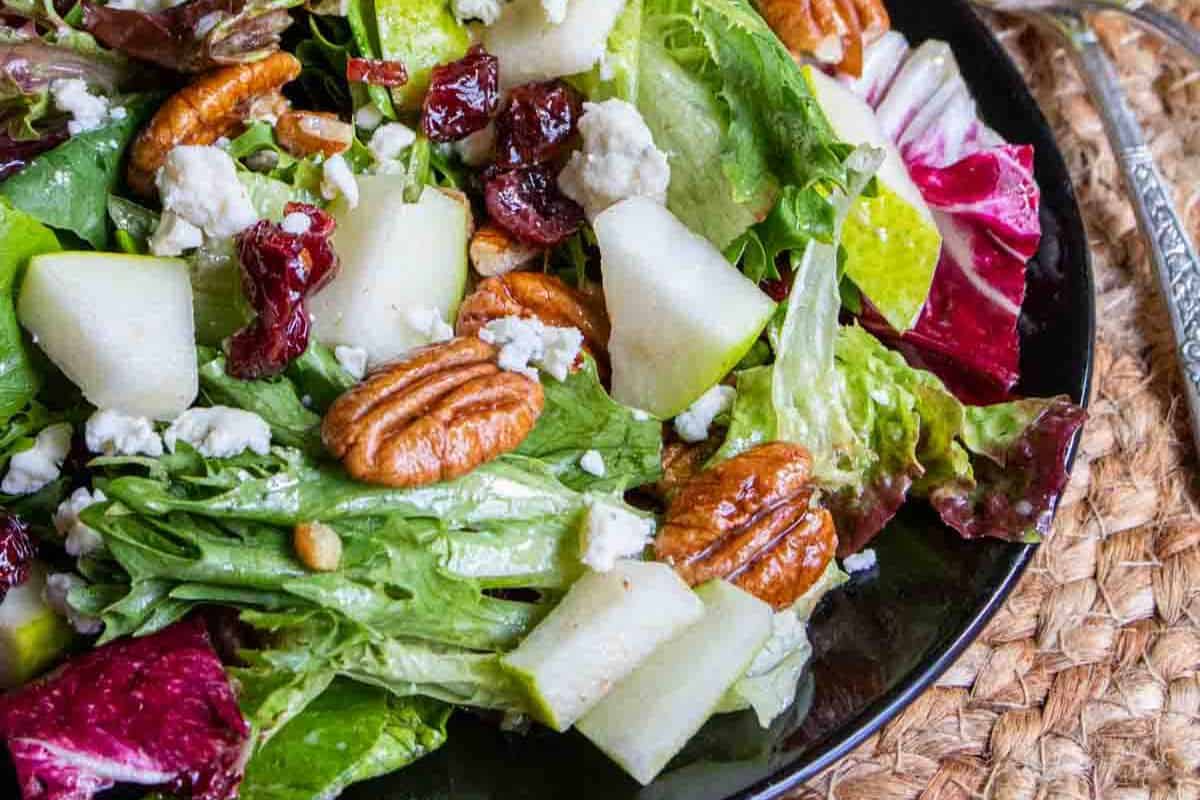 The winter salad with homemade vinaigrette on a black plate.