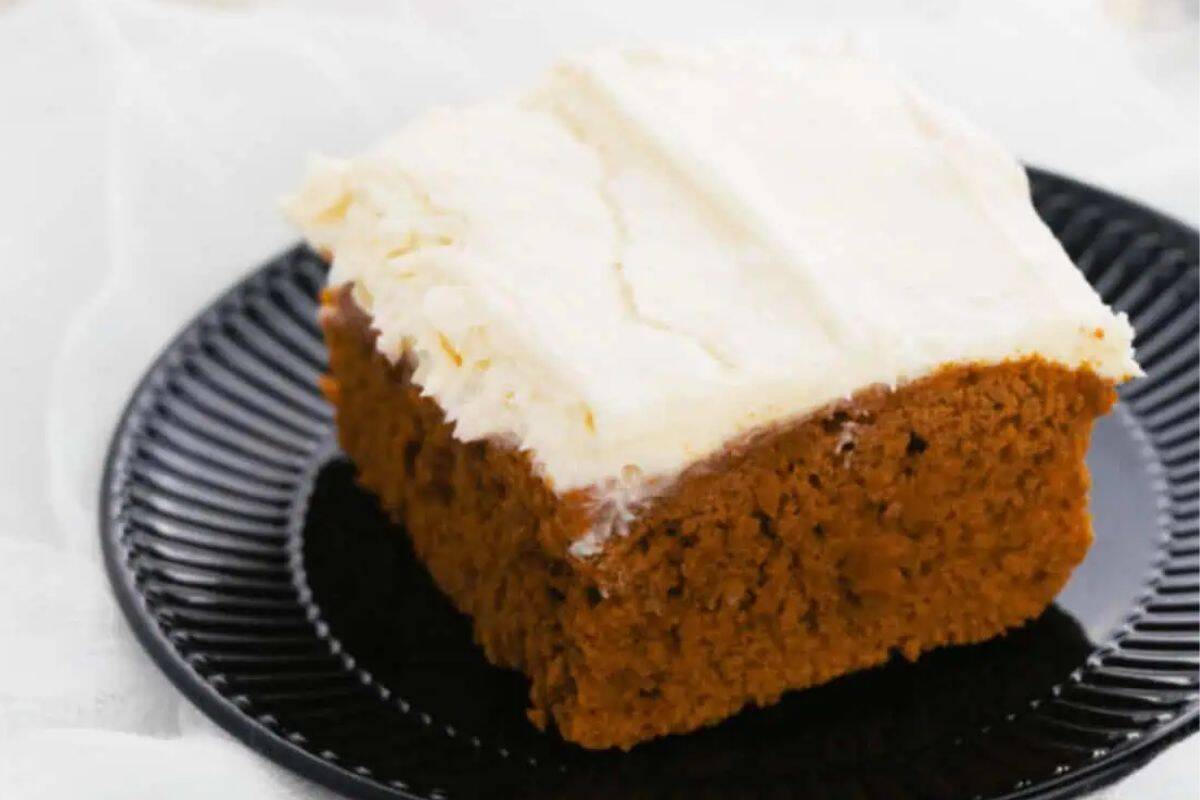 A slice of frosted pumpkin cake sits on a black plate, bringing cozy fall vibes to your table.