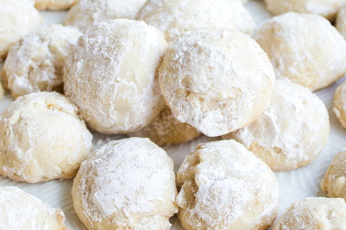 Powdered sugar-coated snowball cookies stacked on a white serving tray.