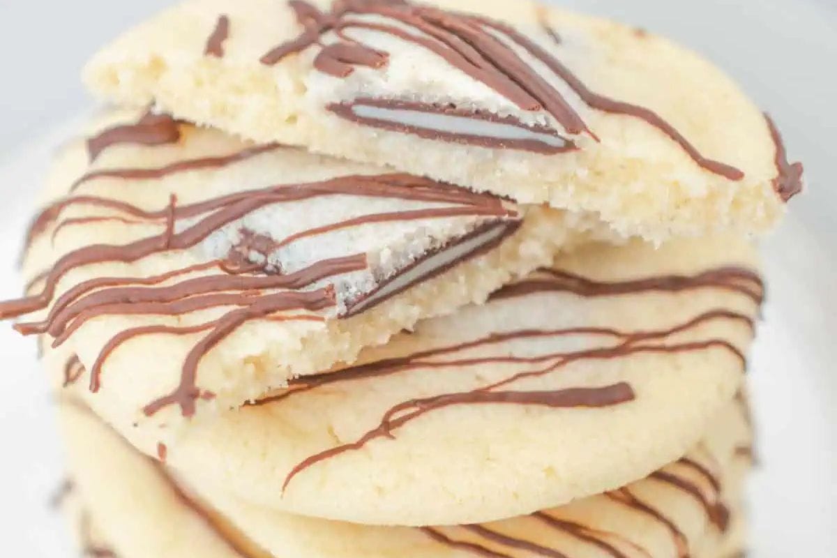 Andes mint-studded chocolate cookies stacked on a white plate, with a candy piece on top and a drizzle of chocolate.