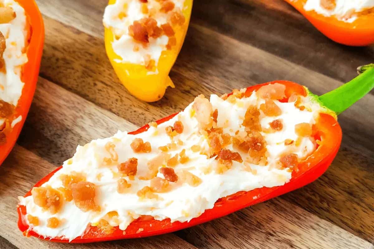 A halved red pepper filled with cream cheese and topped with bacon bits makes an easy stuffed peppers dish—perfect for weeknight dinners. Placed on a rustic wooden surface, it’s a tasty twist on classic stuffed pepper recipes.