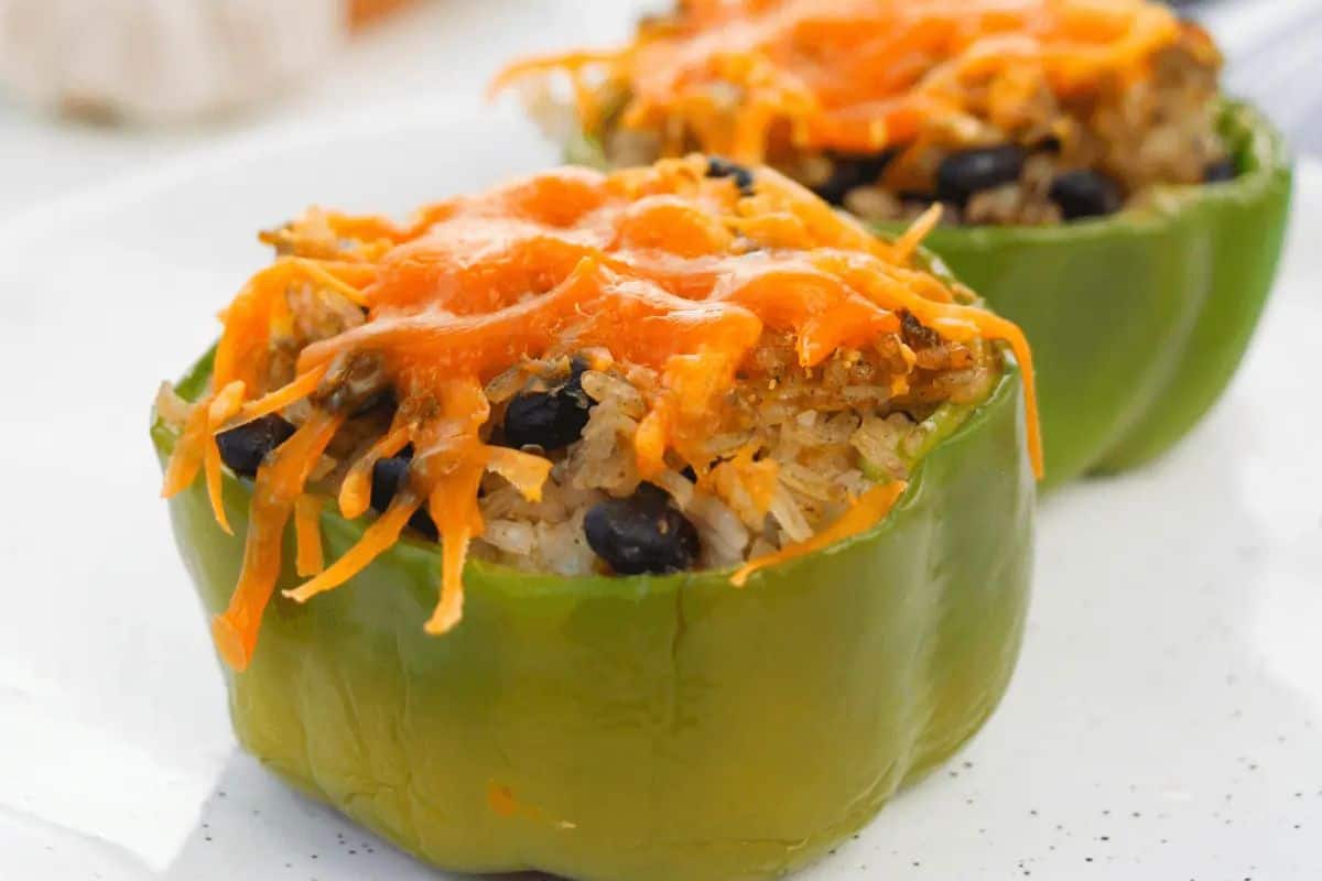 Two green bell peppers stuffed with rice and black beans, topped with melted cheddar cheese on a white plate—perfect for easy stuffed peppers and a comforting weeknight dinner.