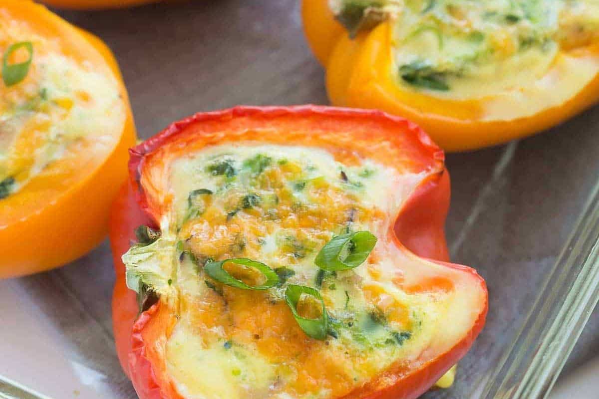 Halved bell peppers filled with a baked egg mixture and topped with chopped green onions—one of the easiest stuffed pepper recipes, perfect for effortless weeknight dinners. Served on a glass baking dish.