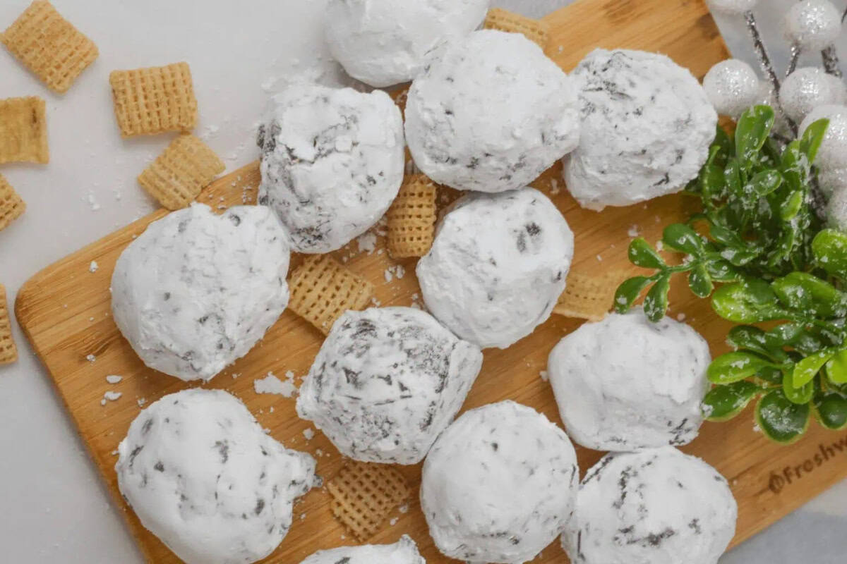 Powdered sugar-coated Chex truffles are arranged on a wooden board with Chex cereal pieces and a small green plant.