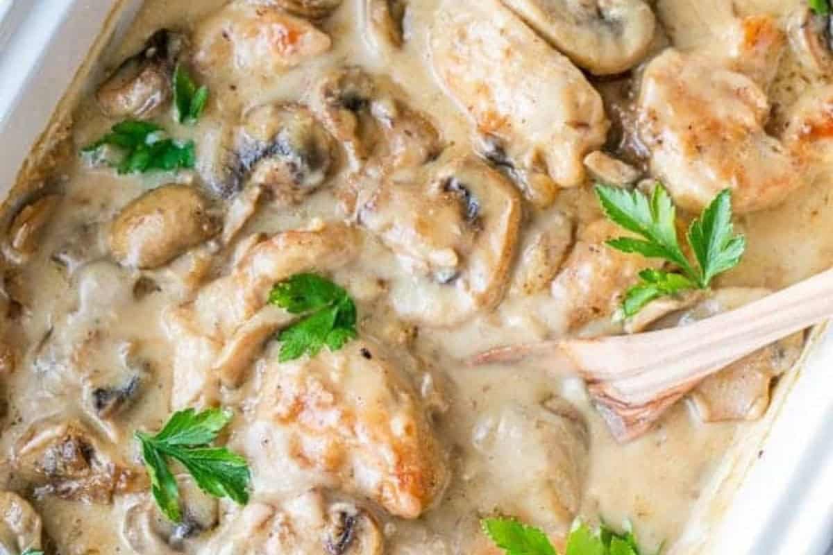 Enjoy the ultimate comfort food with tender chicken breast pieces and mushrooms in a creamy sauce, garnished with parsley—an irresistible addition to your favorite chicken casseroles. Served in a white dish with a wooden spoon.