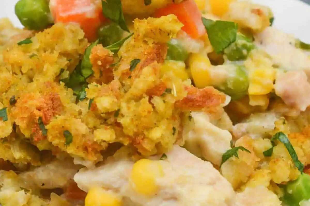 Close-up of a comforting chicken casserole filled with pieces of bread stuffing, tender chicken, corn, peas, carrots, and fresh herbs—a true comfort food classic.