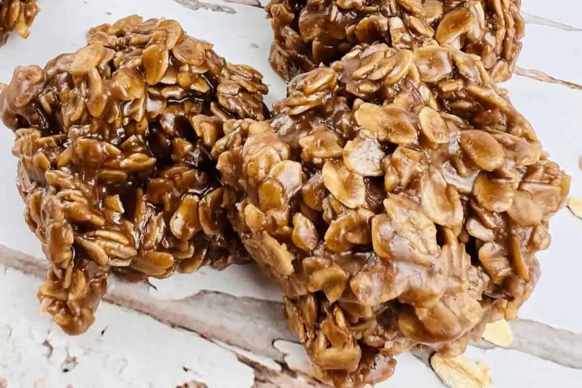 Three no-bake chocolate peanut butter oatmeal cookies are placed on a white wooden surface, showing a textured mixture of oats and chocolate.