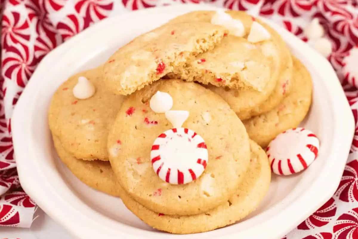 A plate of round Christmas Cookies with white chocolate chips and red peppermint pieces, garnished with peppermint candies, on a white dish.