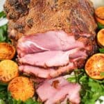 Sliced glazed ham, reminiscent of a copycat HoneyBaked Ham, is beautifully surrounded by halved grilled oranges and fresh parsley on a plate.