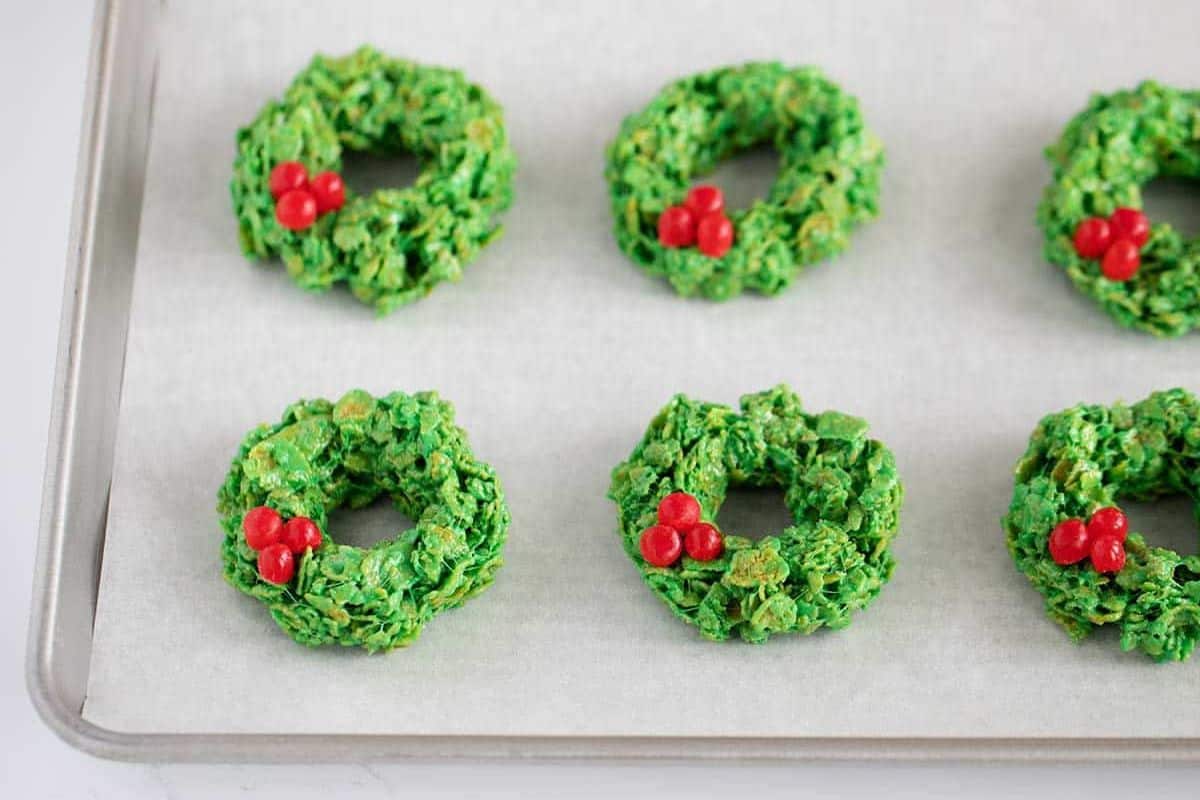 Green cornflake cookies shaped like wreaths with red cinnamon candy “berries.”