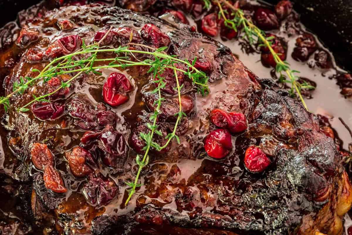 Close-up of a cooked rib roast topped with cranberries and garnished with fresh sprigs of thyme.