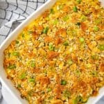A Creamy Chicken Noodle Casserole topped with crushed crackers and sliced green onions sits in a white dish on a marble surface beside a checkered cloth.
