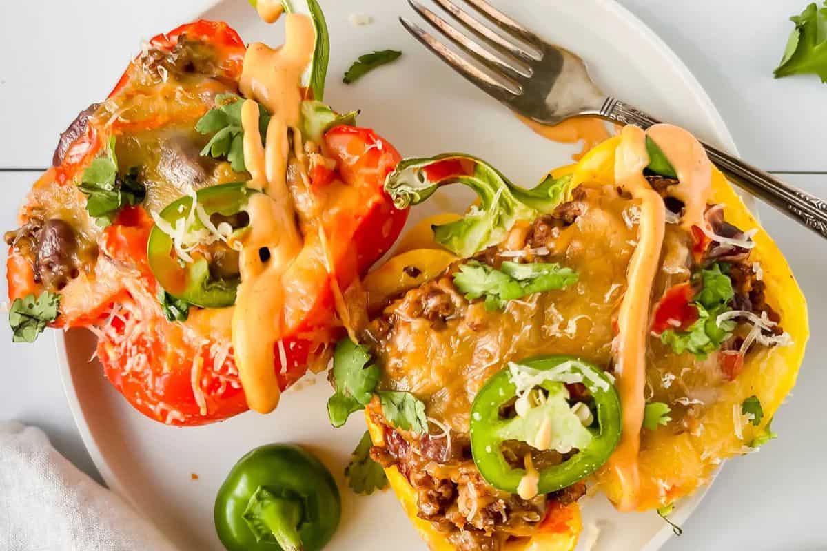 Two stuffed bell pepper halves filled with ground meat, melted cheese, jalapeño slices, chopped herbs, and drizzled sauce on a white plate with a fork—an easy stuffed peppers dish perfect for any weeknight dinner.
