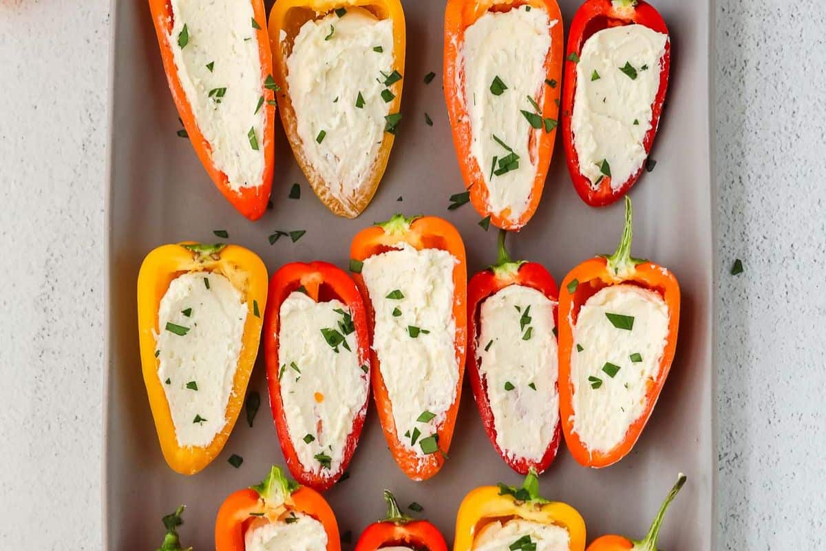 Halved mini bell peppers filled with a creamy white cheese mixture, garnished with chopped herbs, make for one of the easiest stuffed pepper recipes—perfect for effortless weeknight dinners, arranged beautifully on a gray tray.