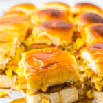 Breakfast sliders crafted with sausage, fluffy scrambled eggs, and creamy cheese, all drizzled with syrup and arranged enticingly.