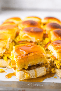 Breakfast sliders crafted with sausage, fluffy scrambled eggs, and creamy cheese, all drizzled with syrup and arranged enticingly.
