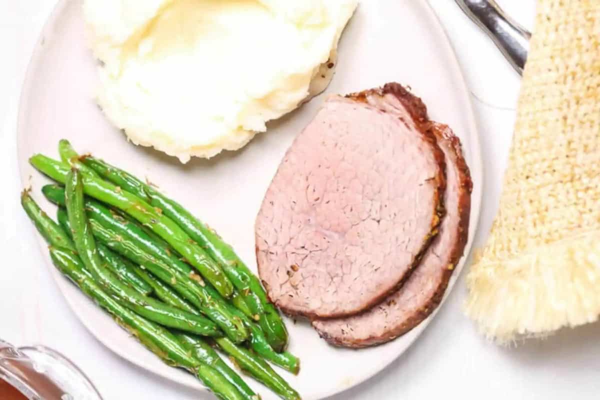 A plate with two slices of roast beef, a serving of mashed potatoes, and seasoned asparagus.