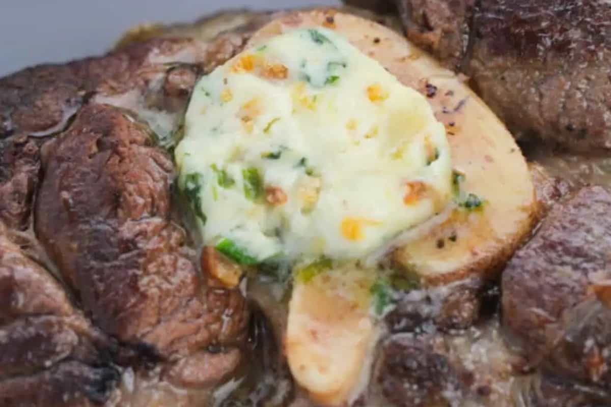 A close-up of a cooked steak topped with a sliced mushroom and a dollop of melting garlic herb butter.