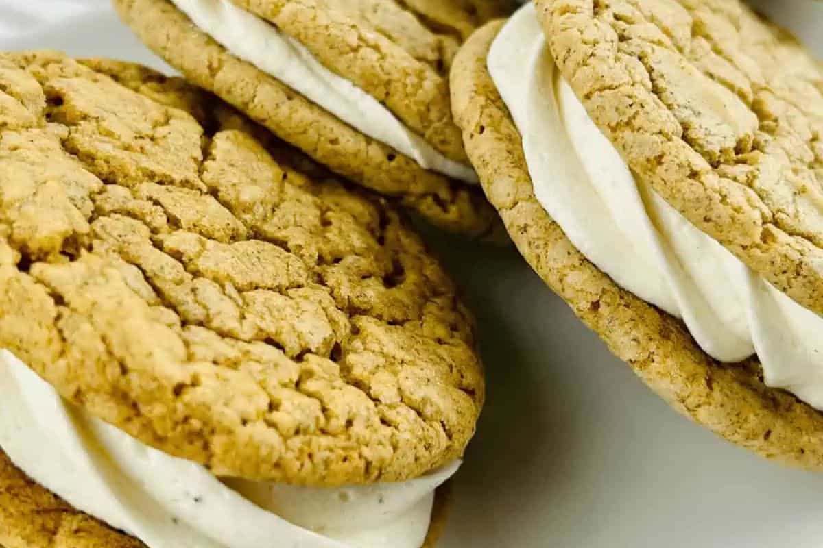 Gingersnap cookies filled with creamy eggnog frosting, stacked on a white tray.
