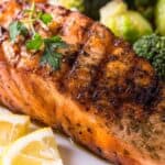Grilled Salmon Salad featuring a succulent salmon fillet garnished with fresh parsley, served with lemon wedges and a side of steamed broccoli and mixed vegetables.