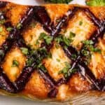 Fish with crosshatch grill marks, garnished with chopped herbs, and served with steamed vegetables in the background.