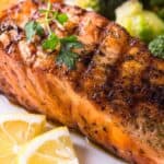 Grilled Salmon fillet garnished with parsley, served with lemon wedges and steamed vegetables including broccoli and carrots, makes this dish a perfect choice for lovers of Grilled Salmon Salad.
