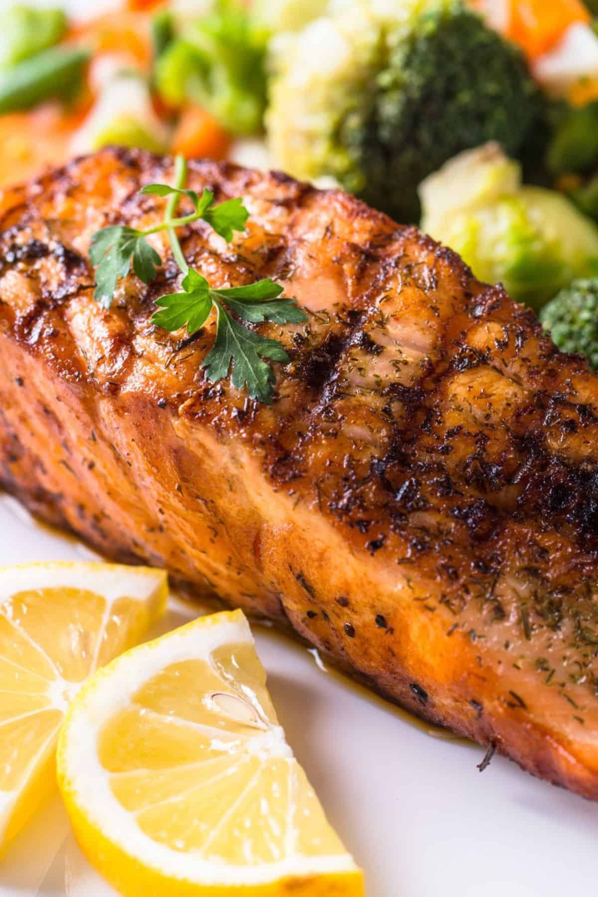 Grilled Salmon fillet garnished with parsley, served with lemon wedges and steamed vegetables including broccoli and carrots, makes this dish a perfect choice for lovers of Grilled Salmon Salad.