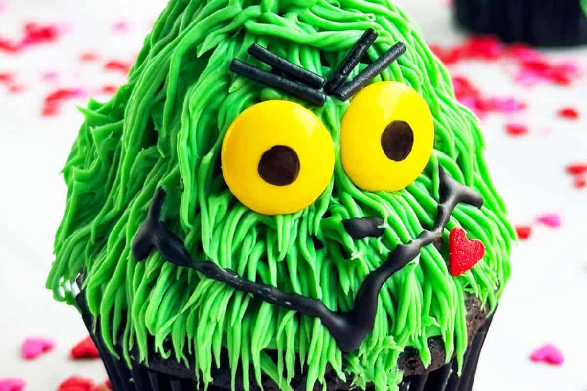 Green-frosted cupcakes made to look like the Grinch with red heart sprinkles and black cupcake liners.