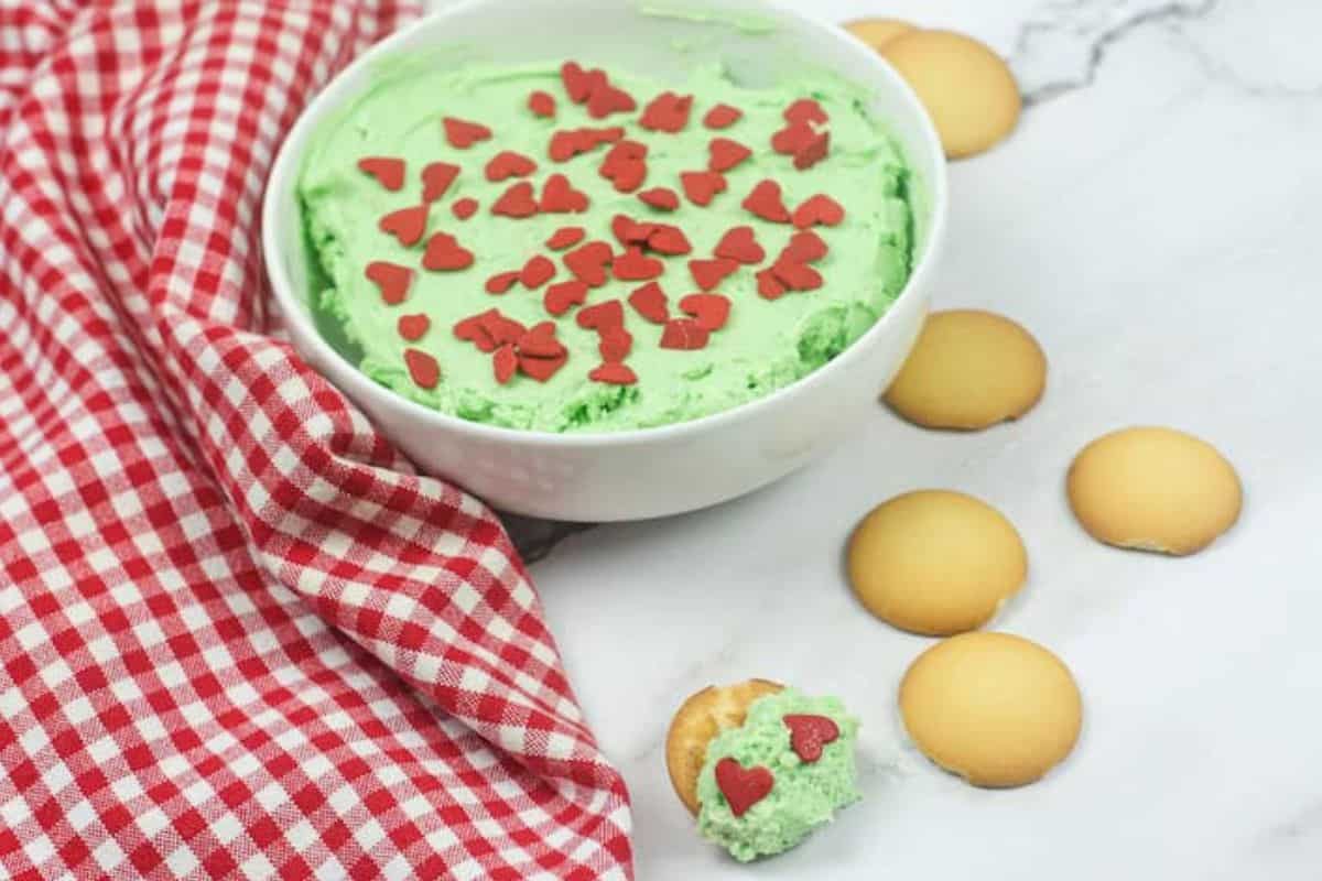 A bowl of creamy green dessert dip surrounded by cookies for dipping.