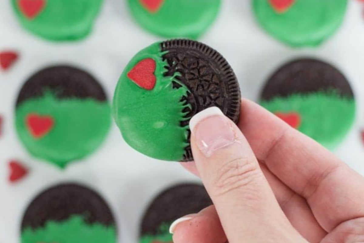 Oreos coated in green candy melts with red heart decorations, lined up on parchment paper.
