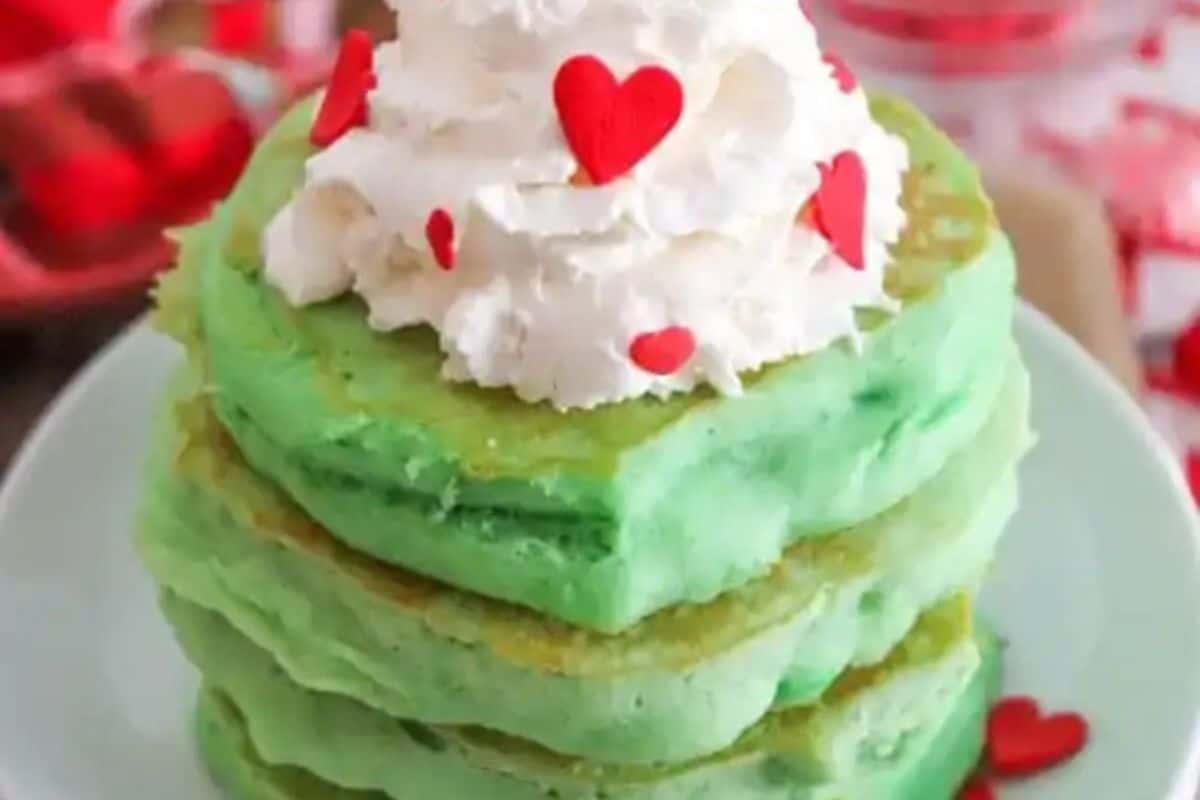 A stack of fluffy green pancakes topped with whipped cream and sprinkles.
