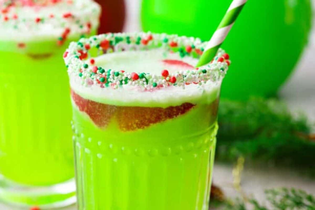 A glass of bright green punch with fizzy bubbles and a strawberry garnish, served with a sprinkle coated rim and a green and white straw.