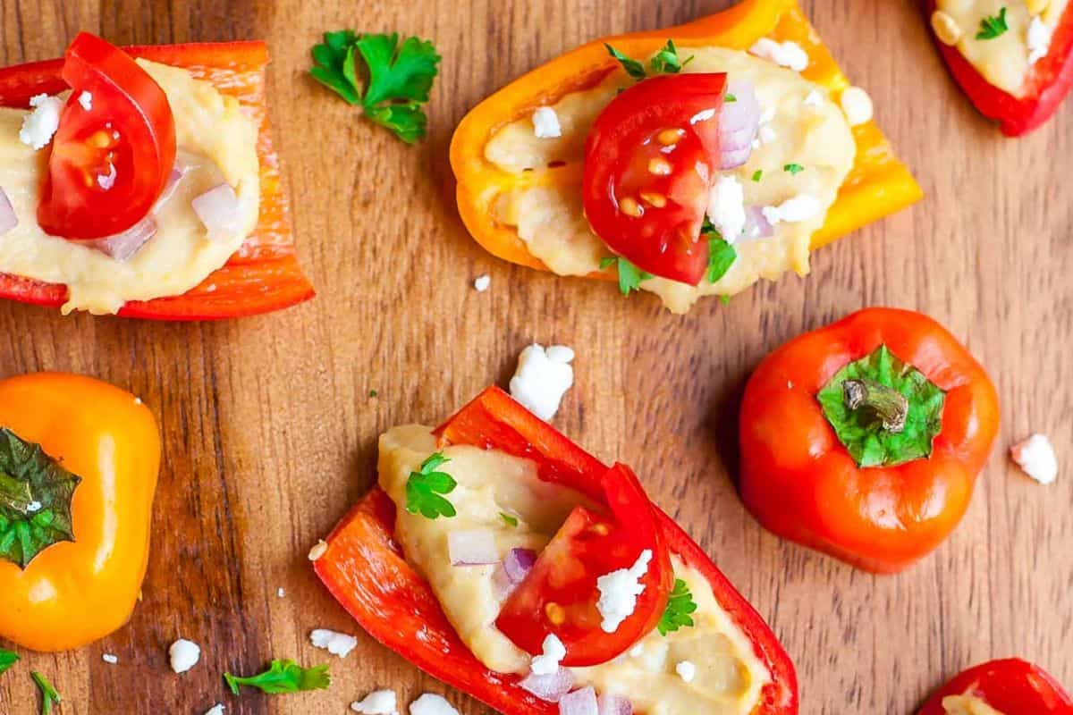 Mini sweet peppers halved and filled with hummus, topped with chopped tomato, red onion, parsley, and feta cheese—an easy recipe perfect for stuffed pepper recipes or quick weeknight dinners.