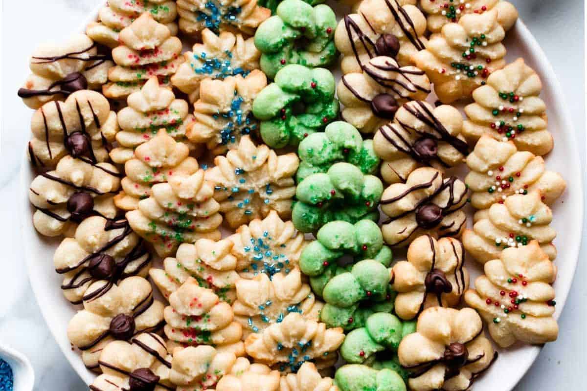 Colorful spritz cookies in festive shapes with red and green sugar sprinkles on a white plate.