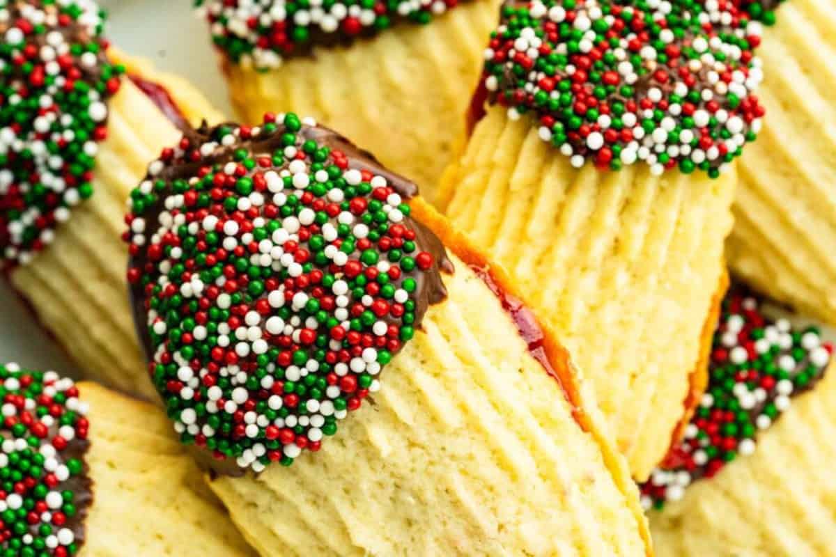 Close-up of Traditional Italian butter cookies filled with raspberry jam, partially dipped in chocolate and decorated with red, white, and green sprinkles.