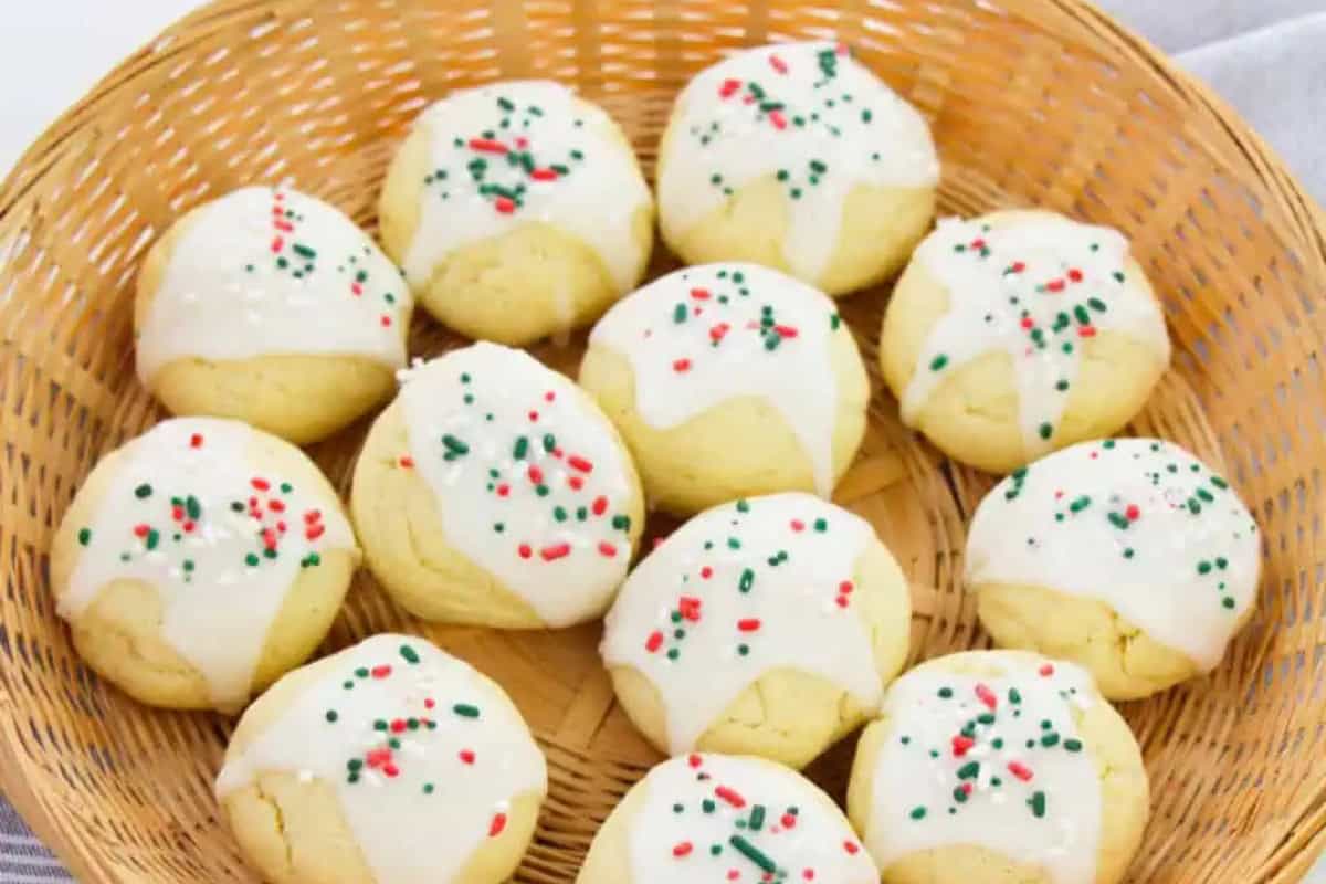A wicker basket filled with round traditional Italian Knot Anginetti cookies, each topped with white icing and festive red and green sprinkles.