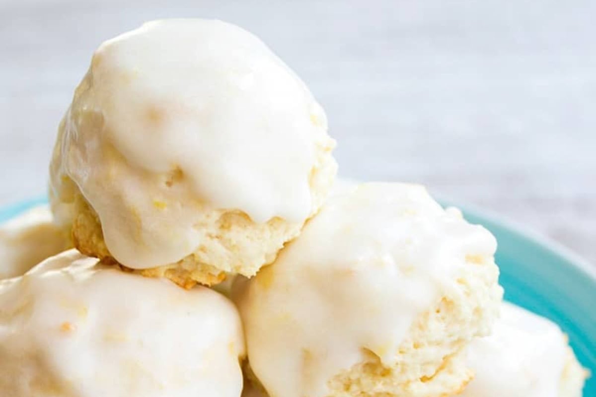 A close-up of glazed Italian lemon drop cookies stacked on a blue plate.