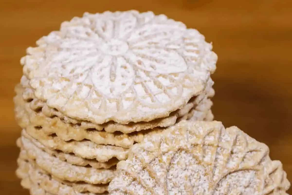 A stack of round, thin Christmas Pizzelle cookies with intricate patterns and a dusting of powdered sugar on top.
