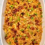 A creamy baked dish in a white rectangular dish, topped with crushed crackers, melted cheese, chopped bacon, and sliced green onions.
