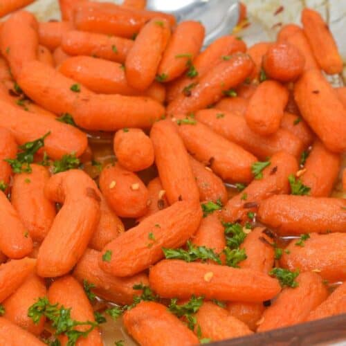 A glass baking dish filled with maple glazed carrots, roasted to perfection and garnished with chopped parsley and red pepper flakes.