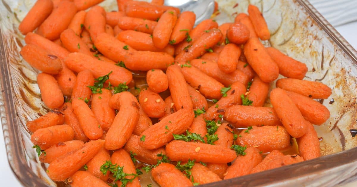 A glass baking dish filled with maple glazed carrots, roasted to perfection and garnished with chopped parsley and red pepper flakes.