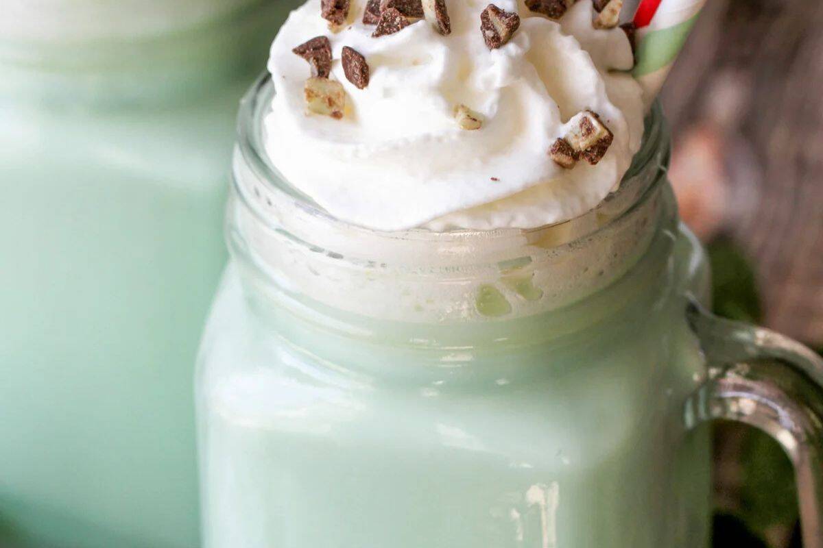 A glass mug filled with a light green mint hot chocolate, topped with whipped cream, chocolate pieces, and a striped straw—perfect for fans of warm drinks or those seeking inspiration beyond classic hot cocoa recipes.