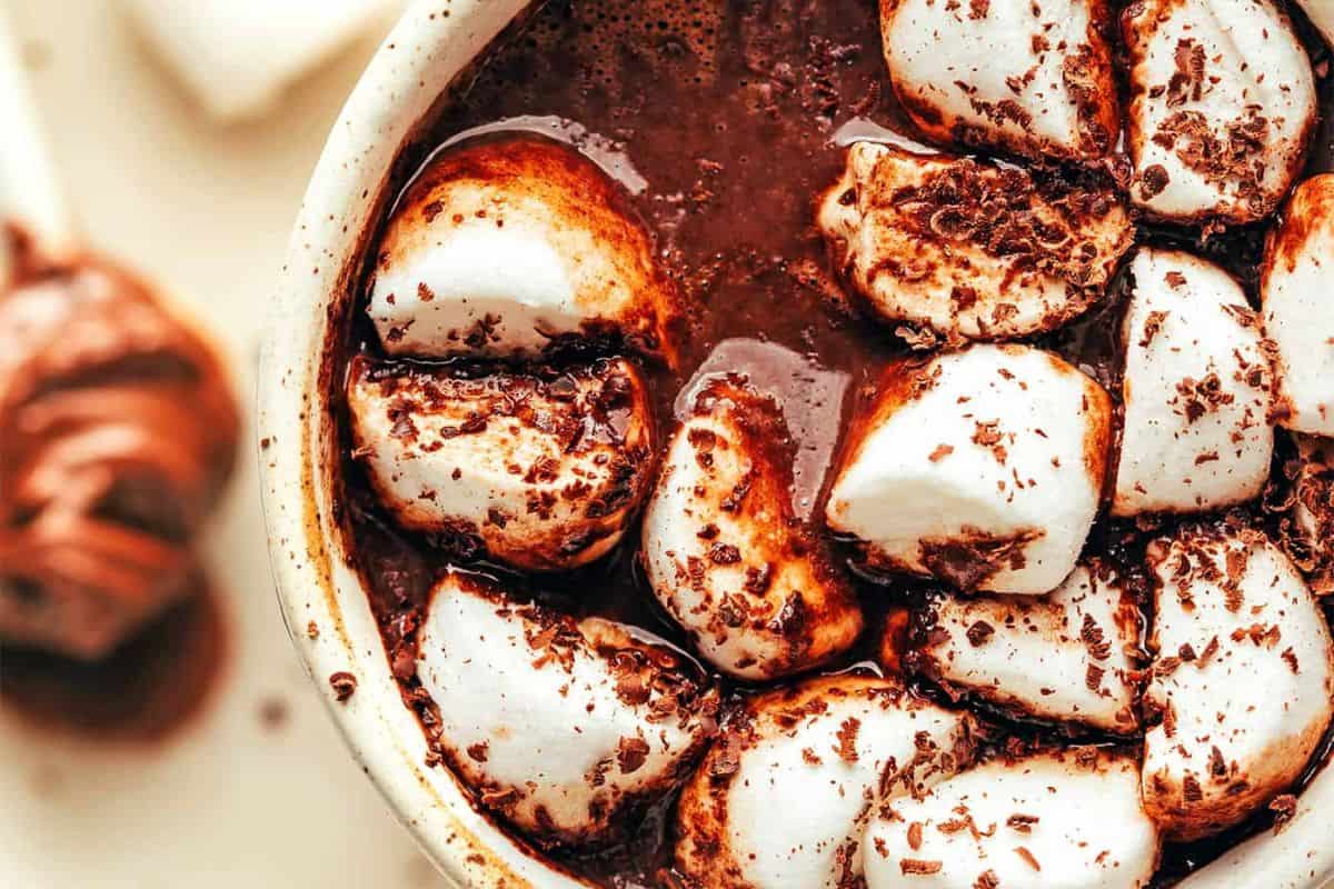 A close-up of a mug filled with creamy hot chocolate, topped with large marshmallows and sprinkled with chocolate shavings—a perfect treat for fans of warm drinks.