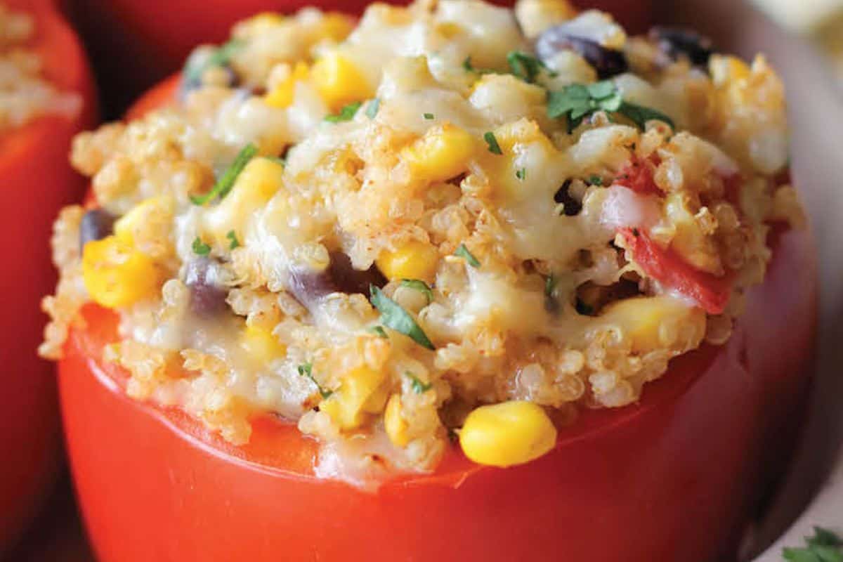 A close-up of a halved tomato stuffed with quinoa, corn, black beans, melted cheese, parsley, and veggies—an easy stuffed peppers twist that's perfect for weeknight dinners.
